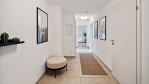 A hallway with a round ottoman, framed pictures on the walls, a door at the end, and a light fixture on the ceiling. - Botanical Design Apart in Erlachplatz (Vienna)