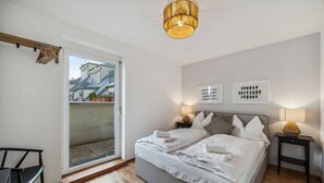 A bedroom with a bed, two bedside tables, a chair, a ceiling light, and a view through a sliding door. - Botanical Design Apart in Erlachplatz (Vienna)