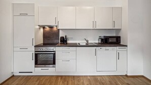 A compact kitchen with white cabinets, a built-in oven, a microwave, and a sink. - Botanical Design Apart in Erlachplatz (Vienna)