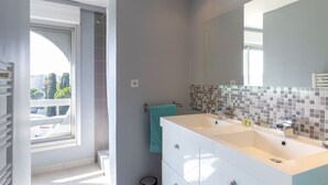 Une salle de bain moderne dotée d’un grand miroir, de deux lavabos et d’une fenêtre laissant entrer la lumière naturelle.