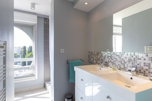 Ein modernes Badezimmer mit einem großen Spiegel, zwei Waschbecken und einem Fenster, das für natürliches Licht sorgt.