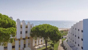 Un hôtel en bord de mer offrant une vue sur l’océan, avec un sentier bordé d’arbres et de nombreux balcons.