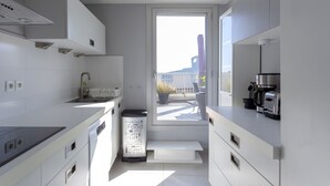 Une cuisine moderne avec des meubles blancs, un lave-vaisselle encastré, une machine à café et une fenêtre donnant sur un balcon.