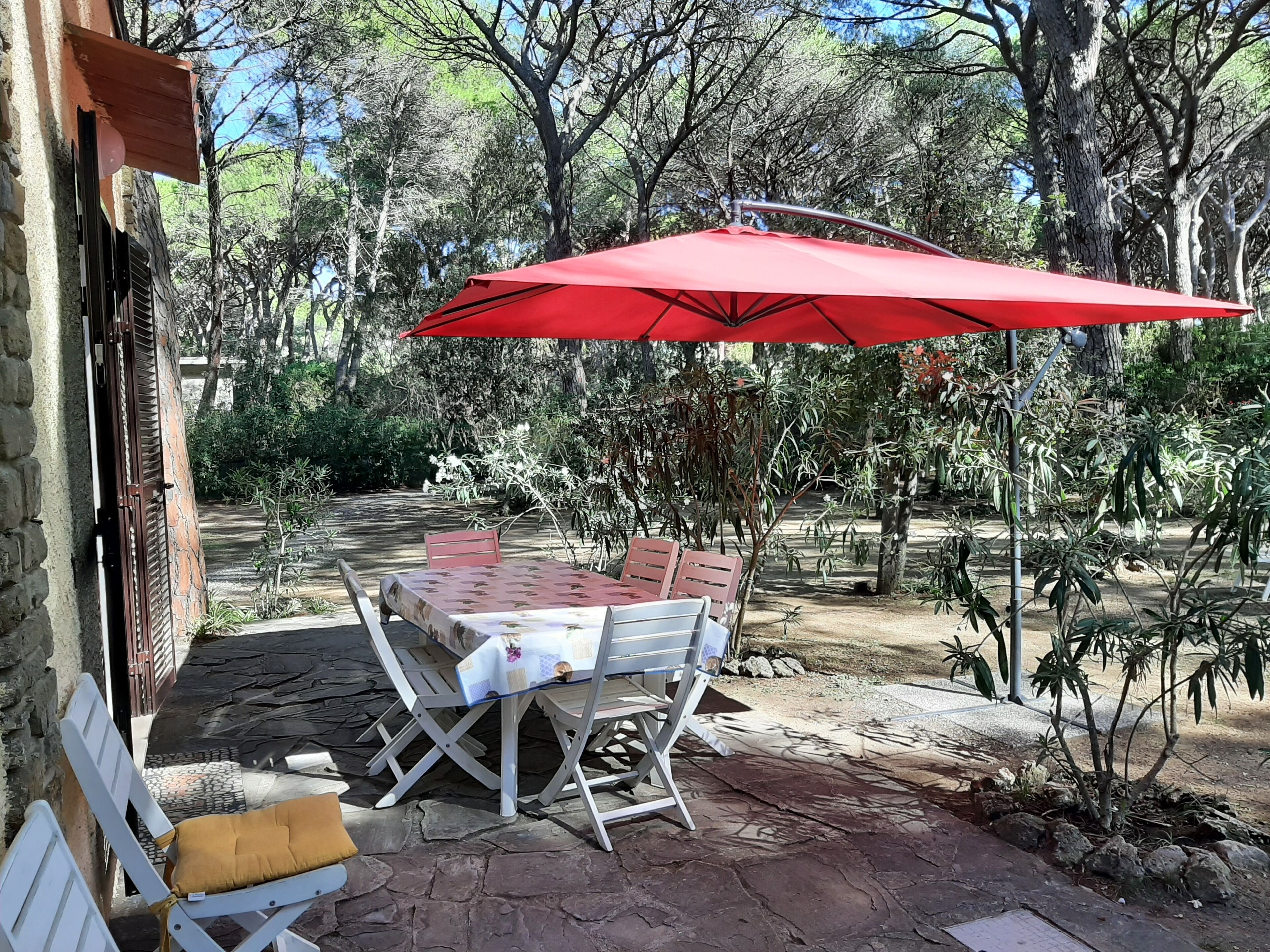 An outdoor patio with a table and chairs, a red umbrella, and a stone pathway.