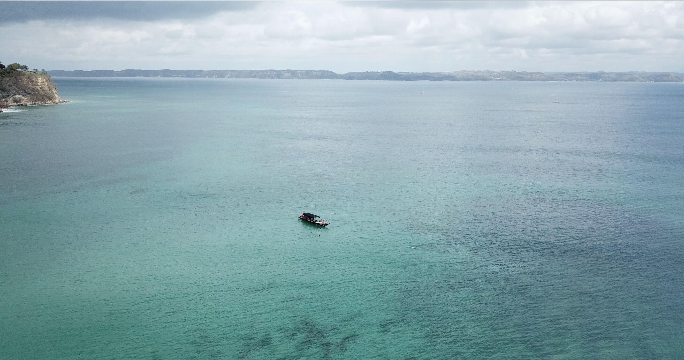 Vista costera con un barco en el agua y un acantilado a la izquierda.