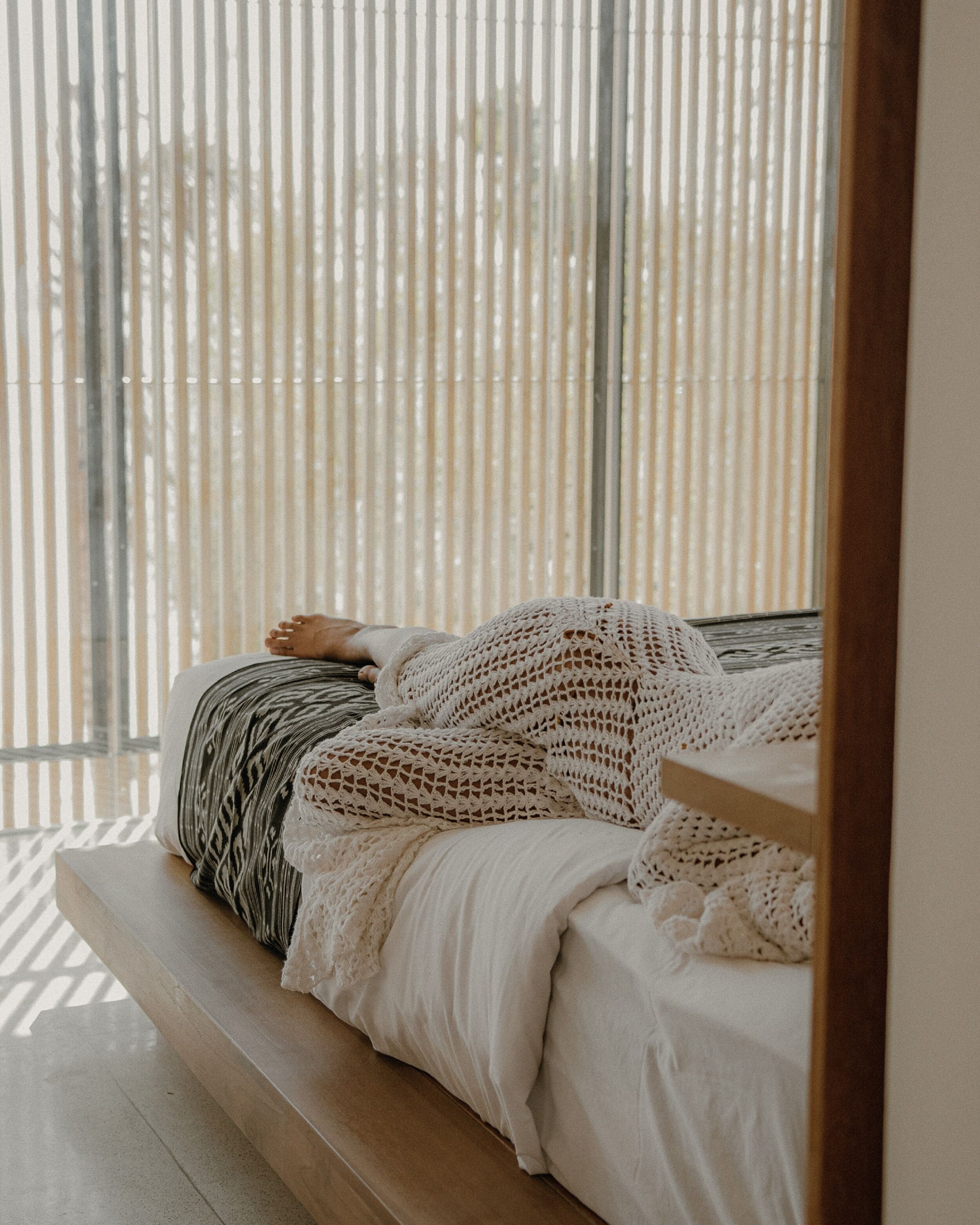 Ein Bett mit einem schwarz-weißen Kissen und einer weißen Strickdecke, am Fußende eine Holzbank.