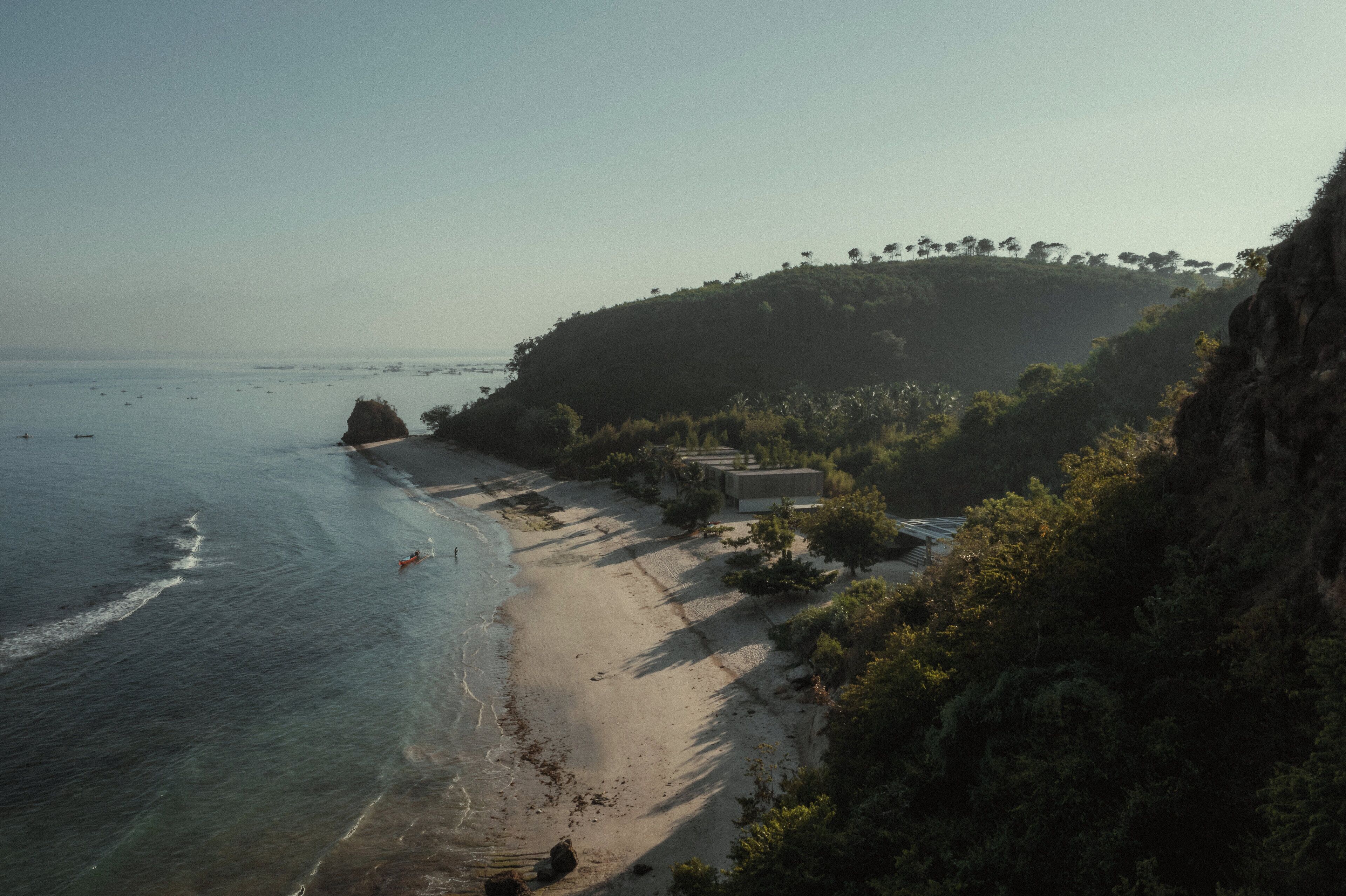 A coastal beach with a rocky outcrop, a small building, and dense vegetation.