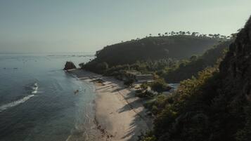 A coastal beach with a rocky outcrop, a small building, and dense vegetation.
