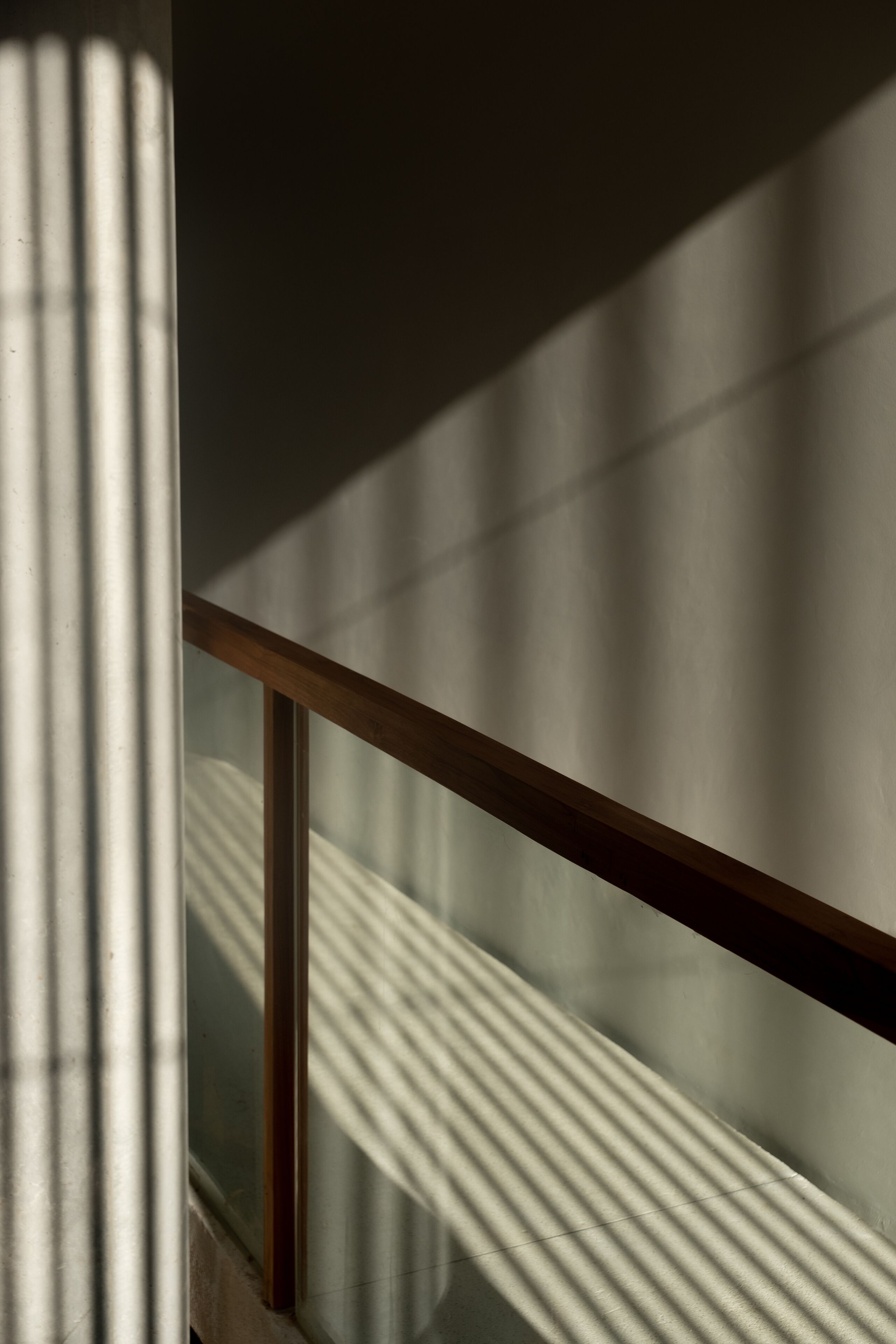 A close-up of a wooden railing with vertical shadows cast on a textured wall.