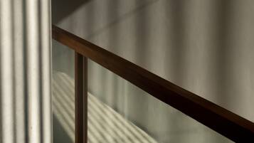 A close-up of a wooden railing with vertical shadows cast on a textured wall.