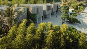 A modern building with a unique architectural design, surrounded by lush greenery and a sandy area. - Innit Lombok (Jerowaru)