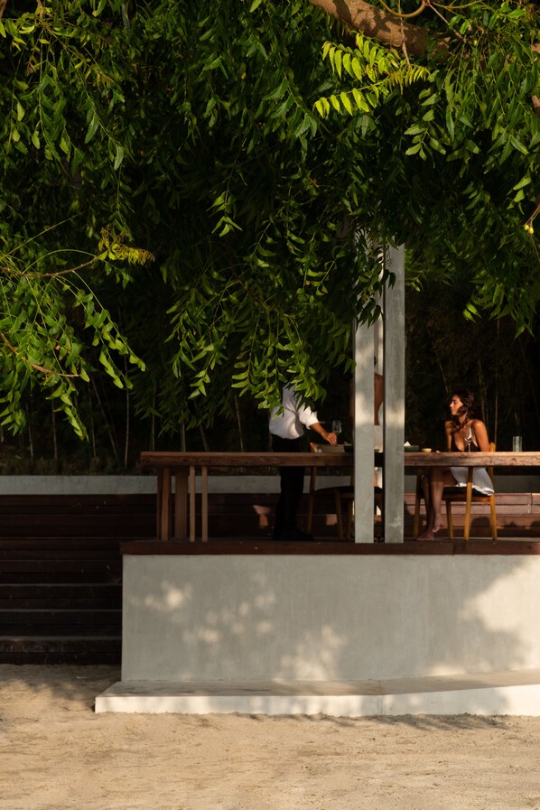 Un área de comedor al aire libre con un banco y una mesa de concreto, rodeada de follaje denso.