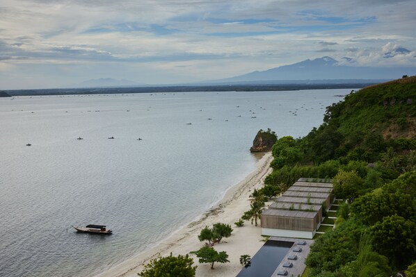 A coastal view with a beach, boats, and a mountain in the background.