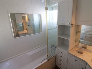 Une salle de bain dotée d’une douche à parois de verre, d’un miroir et d’un meuble-lavabo avec un plan de travail en marbre.