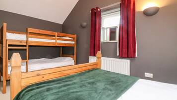 A room with a bunk bed, a single bed, a window with red curtains, a wall-mounted light, and a radiator.