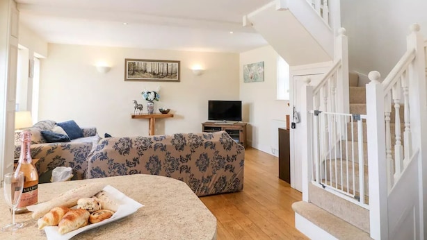 Una sala de estar con un sofá, una mesa baja con croissants, un televisor y una escalera.