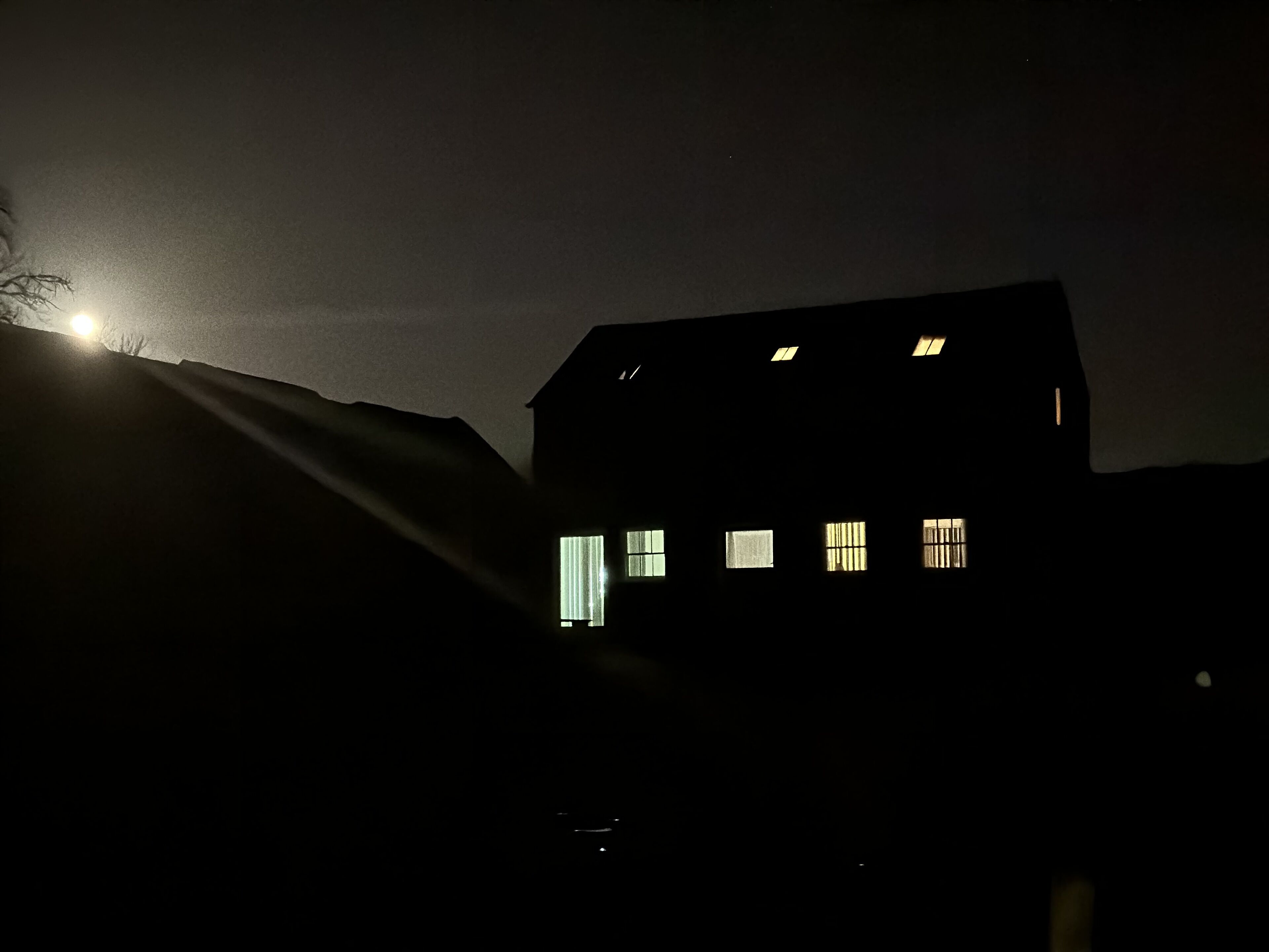 A dark silhouette of a house with multiple windows, a visible door, and a moon in the background.