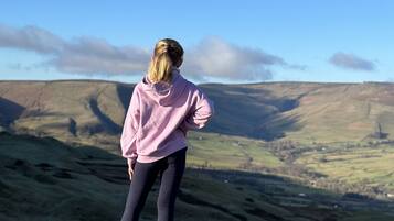 A person standing on a grassy hill overlooking a valley with rolling hills and a clear blue sky.