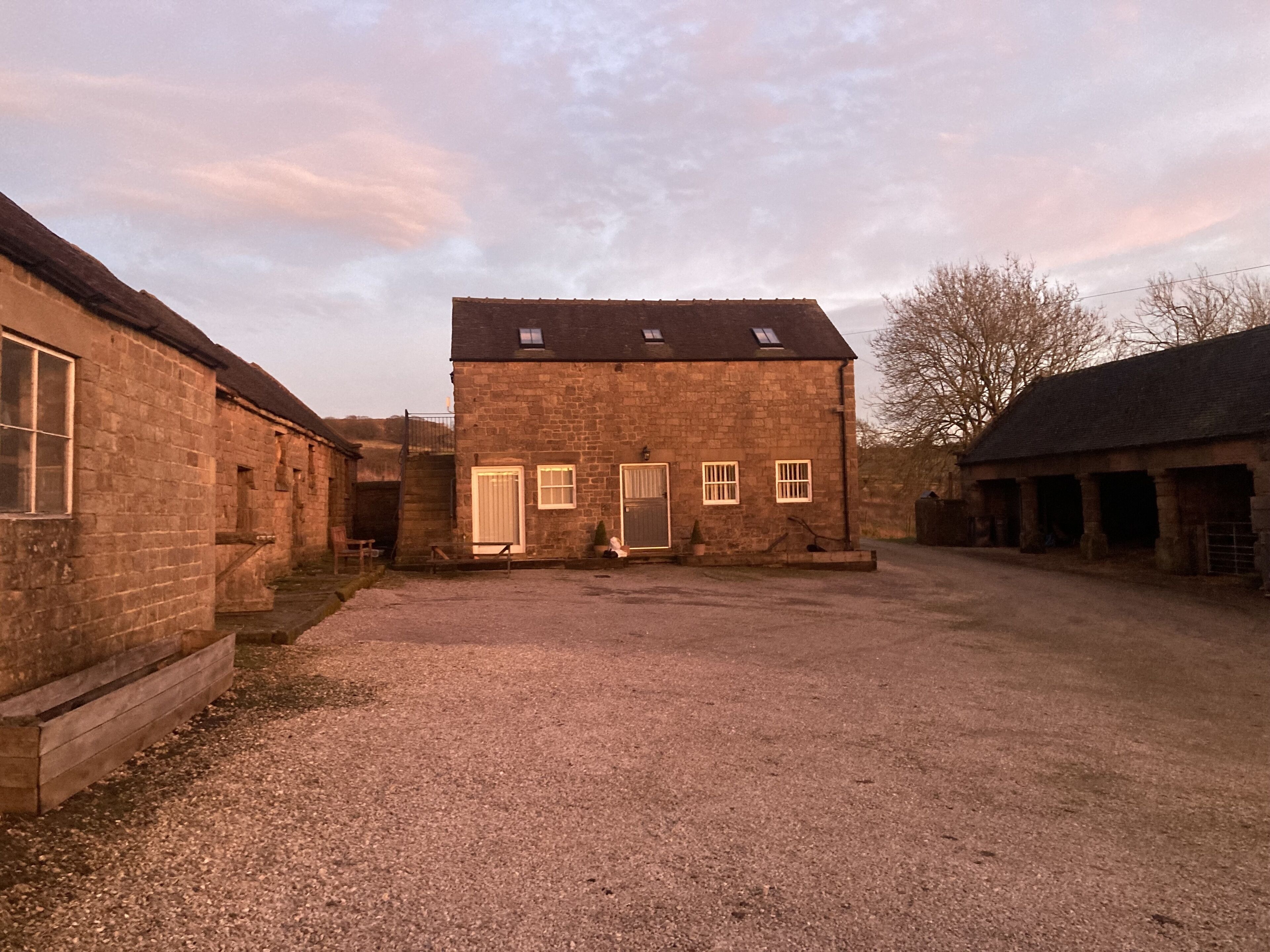 A stone building with a gravel driveway, a wooden bench, and a door with a window.