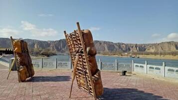 A sculpture of a human figure with a ladder, set on a paved area with a river and mountains in the background.