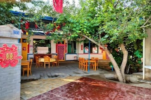 An outdoor dining area with tables and chairs, a tiled floor, and a tree providing shade.