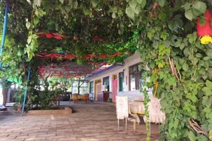 An outdoor patio area with brick flooring, tables, chairs, and a covered seating area with a red and white canopy.