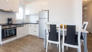 A modern kitchen with white cabinetry, a built-in oven, and a coffee maker. There is a dining area with a white table and black chairs. - 2 bedroom stunning apartment in Makarska (Makarska)