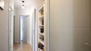 Un pasillo estrecho con suelo de madera, paredes blancas y un armario blanco con estantes.