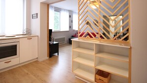 Una cocina moderna con armarios blancos, horno empotrado y encimera de madera. Se aprecia un amplio ventanal con cortinas translúcidas y una estantería de madera con diseño geométrico.