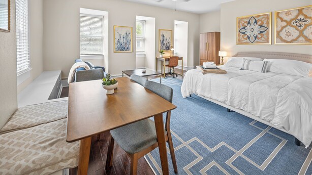 A hotel room with a bed, a desk, a chair, a ceiling fan, and artwork on the walls. - Scenic South Main Apartment with Breathtaking Views for 3 Guests (Saint Charles)
