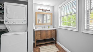 A laundry area with a washer and dryer, a vanity with a mirror, and a window with blinds. - Scenic South Main Apartment with Breathtaking Views for 3 Guests (Saint Charles)