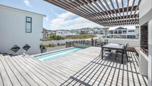 A wooden deck with a pool, outdoor furniture, and a pergola. - Sandbanks Villa (Yzerfontein)