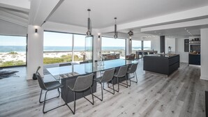 A modern kitchen with a large island, large windows, and a view of the beach. - Sandbanks Villa (Yzerfontein)