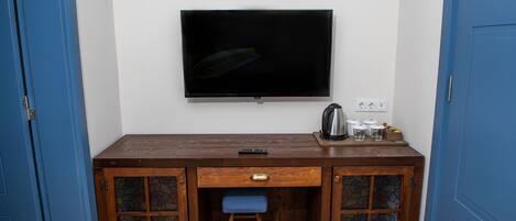 A small room with a wooden desk, a television mounted on the wall, and a blue door.