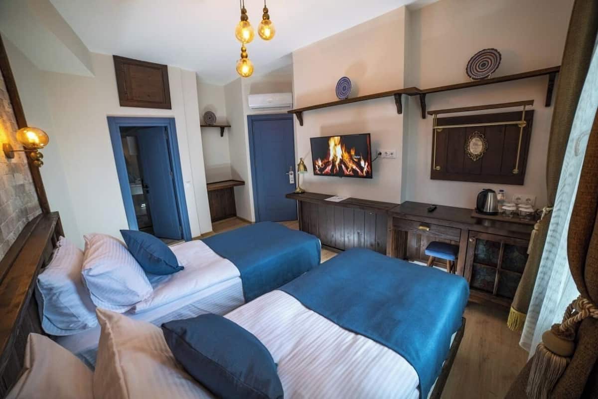 A hotel room with two beds, a desk, a TV, and a fireplace.