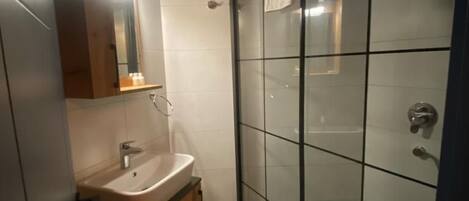 A bathroom with a glass shower enclosure, a sink with a mirror, and a tiled floor.