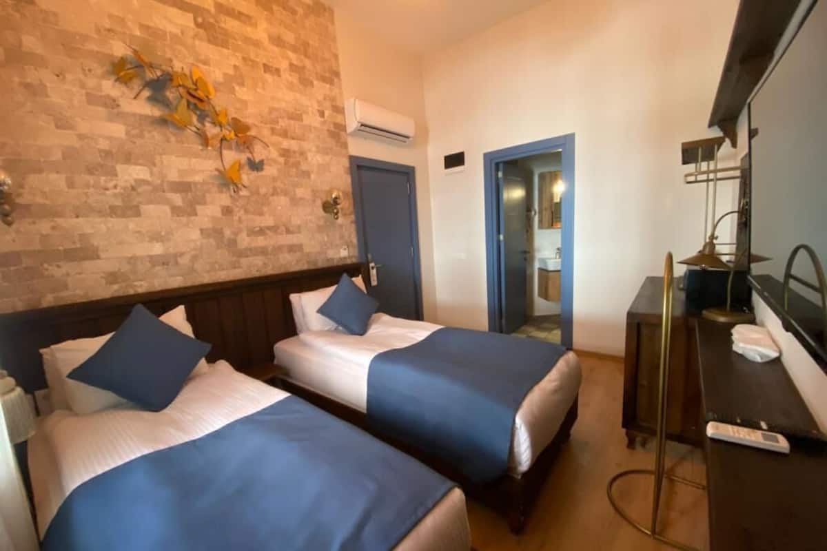 A hotel room with two beds, a brick wall, a mirror, a desk, and a TV.