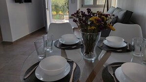 A dining area with a table set for four, a vase with flowers, and a view of the outdoors. - Elia Luxury Apartments Estd 2022 (Preveza)