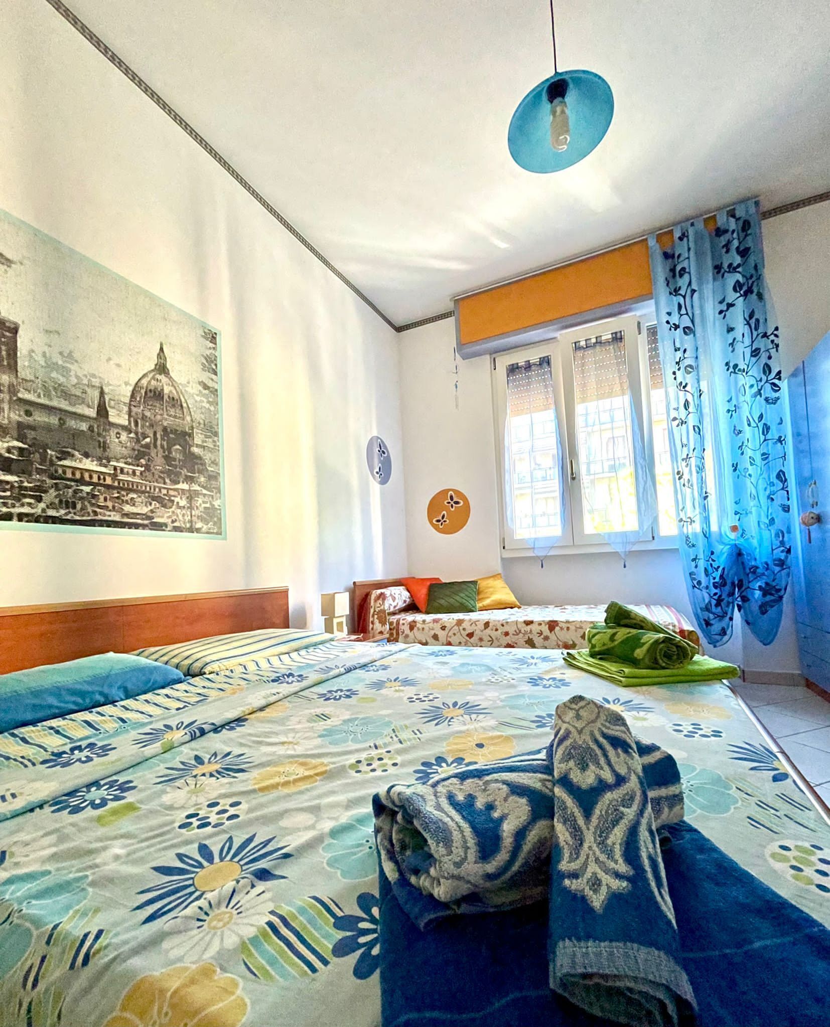 A bedroom with a bed, a window with curtains, a wall clock, and a framed picture.