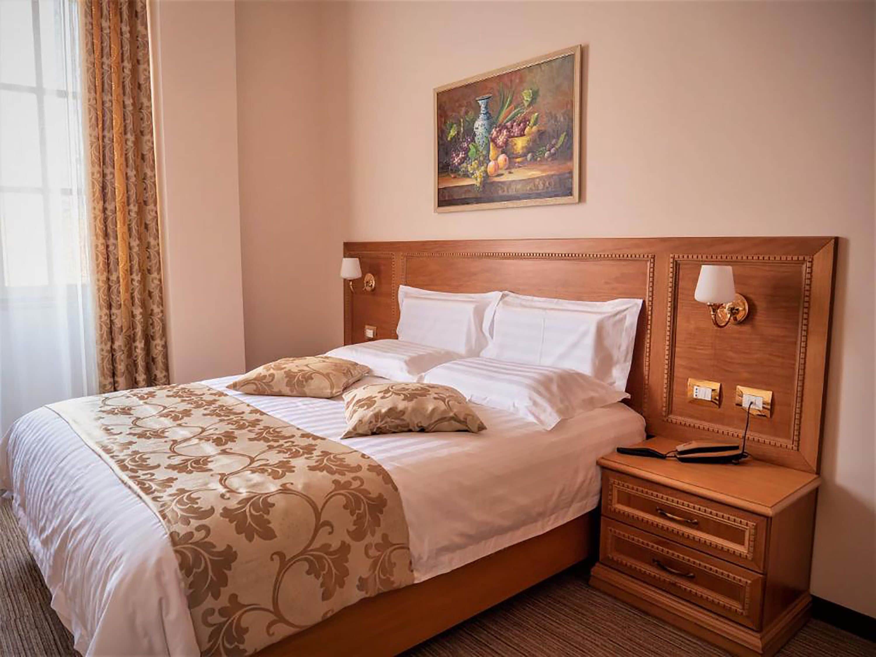 A hotel room with a large bed, a wooden headboard, two bedside tables with lamps, and a painting on the wall.