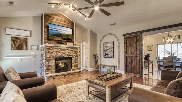 A spacious living room with a stone fireplace, leather sofas, a wooden coffee table, and a ceiling fan.
