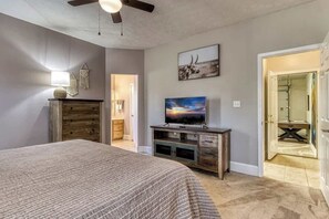 A bedroom with a bed, a TV on a wooden stand, a ceiling fan, and a door leading to a bathroom. - 4BR Mtn Retreat w/ Game Room, Screened Porch, & Hot Tub + Seasonal Pool (Sevierville)