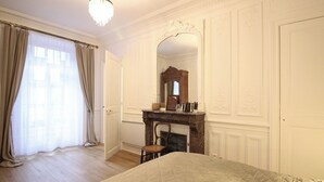 A bedroom with a large bed, a fireplace, a mirror, and a window with curtains. - Mont-Dore Center: Beautiful T2 Apartment with Wifi Near the Thermal Baths (Mont-Dore)