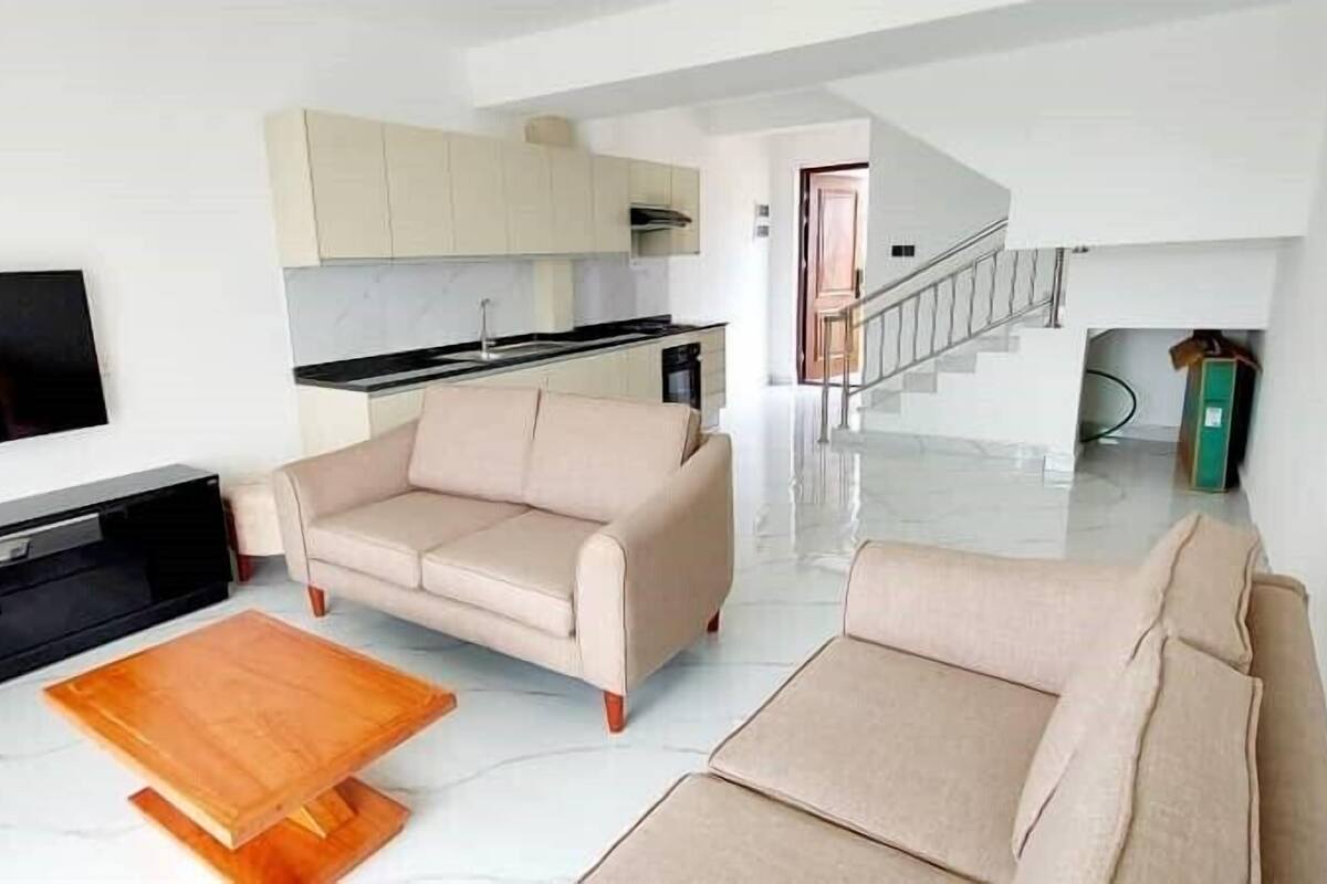 Uma sala de estar moderna com televisão de tela plana, sofás bege e uma mesa de centro de madeira.