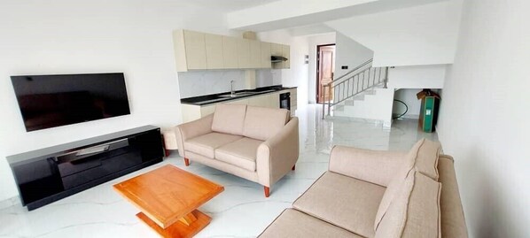 Una sala de estar moderna con un televisor de pantalla plana, sofás color beige y una mesa de centro de madera.