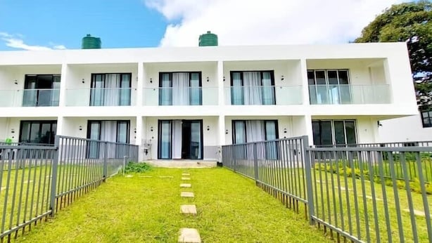 A modern multi-story building with balconies, a central entrance, and a well-maintained lawn.