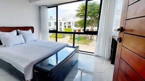 A bedroom with a bed, a bedside table, and a large window offering a view of the outside.