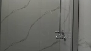 A bathroom with a glass shower enclosure and a marble-tiled wall.