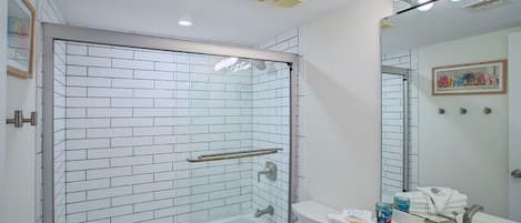 A modern bathroom with a glass-enclosed shower, white tiled walls, a white sink, and a mirror with lights above it.