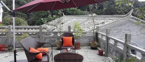 A balcony with wicker chairs, a red umbrella, and potted plants.